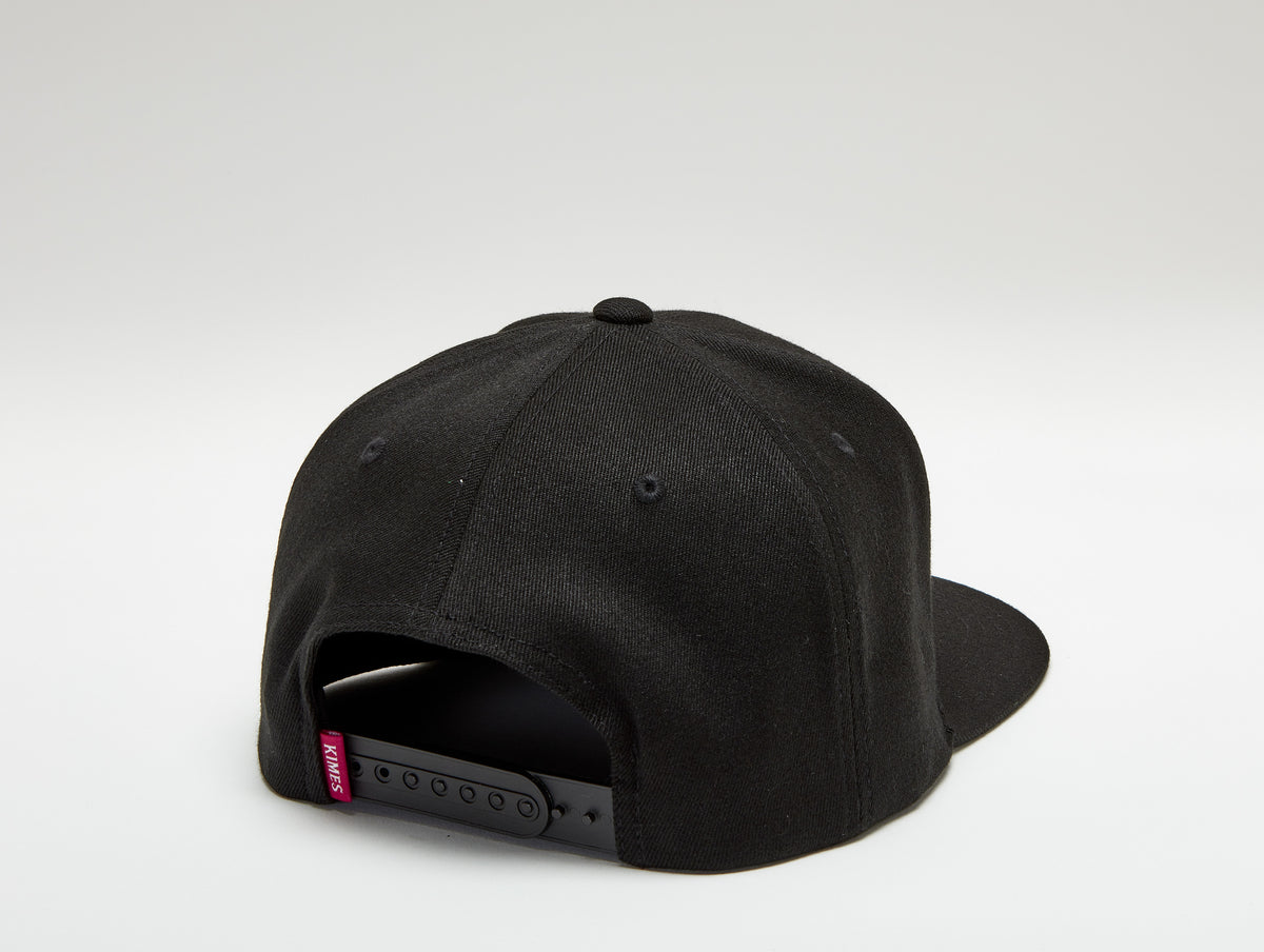 Kimes Ranch Arched Trucker Hat in black with a red Kimes Ranch logo tag on the adjustable strap