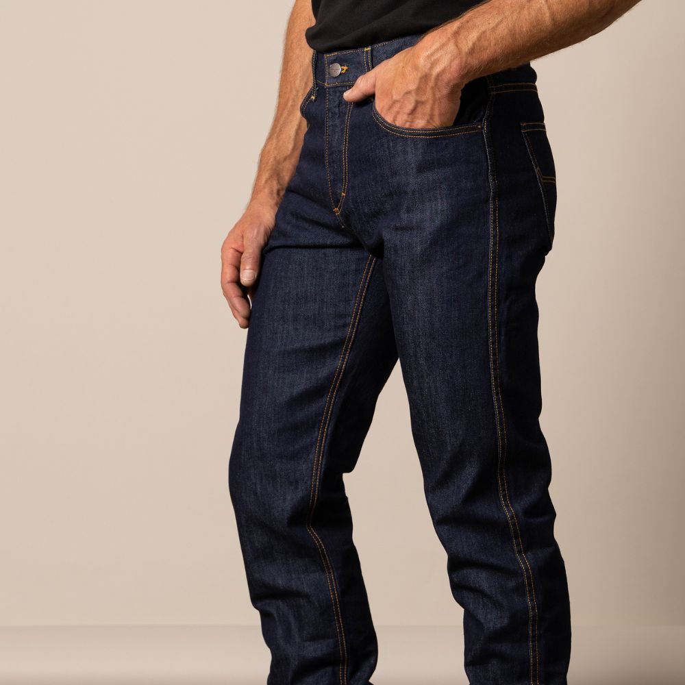 Man wearing Kimes Ranch Cal jeans in dark indigo 100% cotton denim with a straight fit and higher rise. The jeans feature clean double-stitched seams and an integrated knife pocket, blending classic Western style with modern craftsmanship