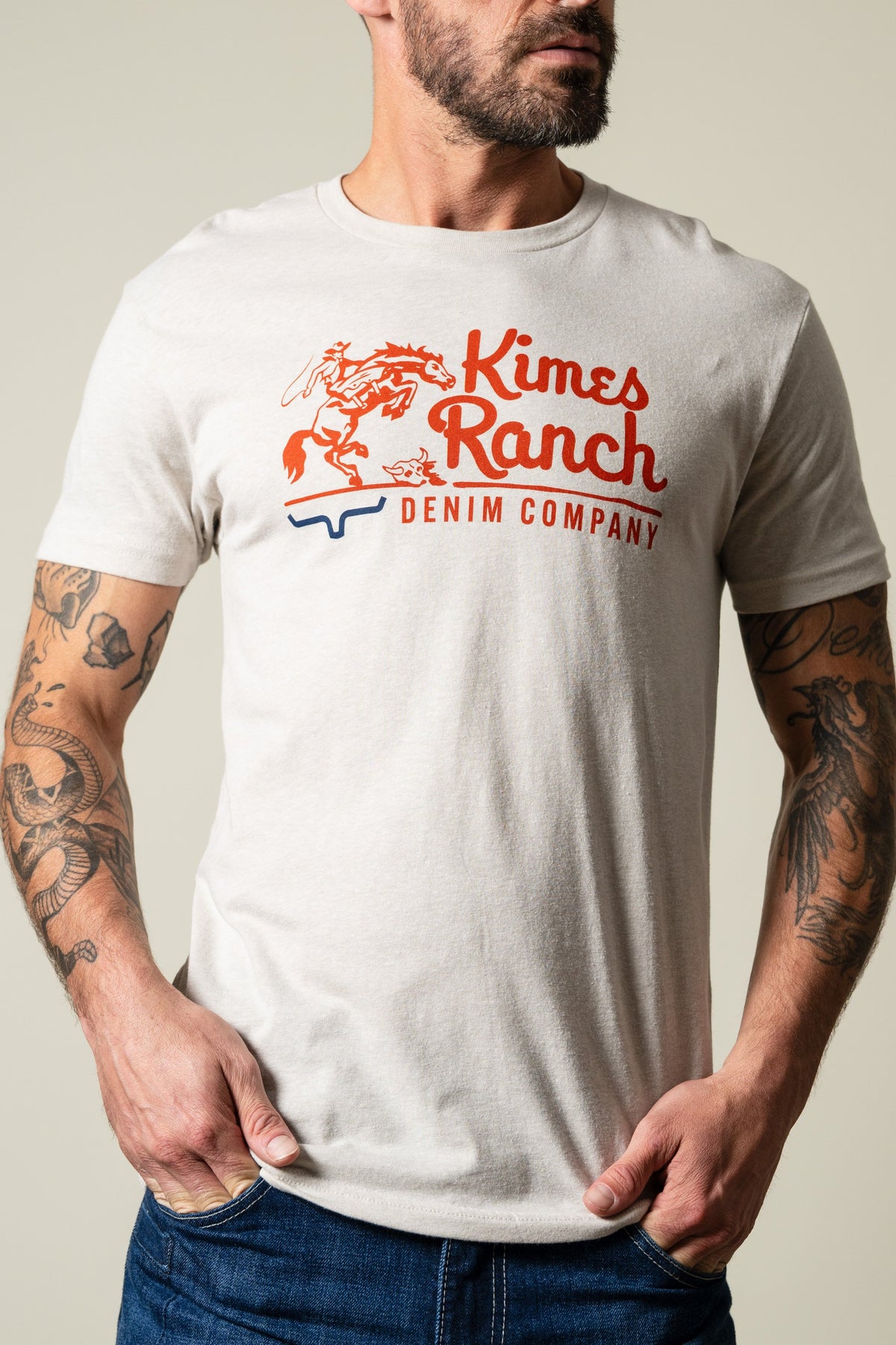 Kimes Ranch Davona Dale Sand short sleeve tee with orange horse rider graphic and 'Kimes Ranch DENIM COMPANY' text; #color_sand