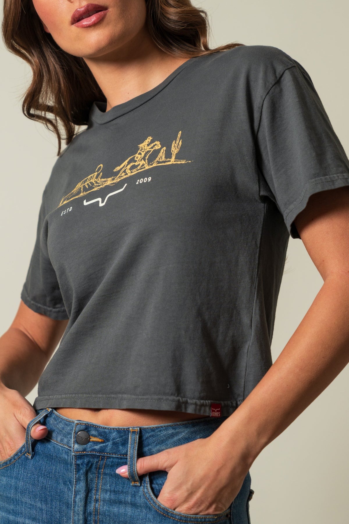 Kimes Ranch Go West cropped tee in Pepper, front view showing short sleeves and a gold graphic with riders, cacti, and text; #color_pepper